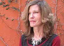 Portrait of lady looking off camera left, wearing necklace. Stands in front of red wall.