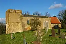 A stone church seen from the south; from the left is a broad squat plain tower, then a nave with a slate roof and two windows, and at the right a small chancel with a red tiled roof