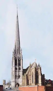 A church seen from the east with a sandstone polygonal apse, and a very tall limestone steeple.