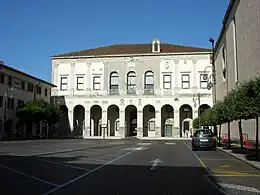 Facade of imposing building with Greek columns. Large colored banners hang from the building's top. A crowd of people is in front.