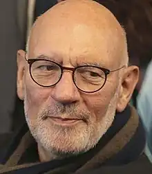 Bearded man with spectacles, bald with short white beard, and a half smile.