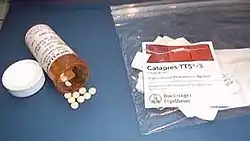 Little white pills on a counter, next to a pill bottle and labels