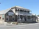 Double-story building with hipped roof. 3 bays, symmetrical.
Double verandah, plain roof, returned, with plenty of ornamental cast-iron detail.
Hoods and keystones above windows.
Front door 6 panels, leaded fanlight, stained glass.
Sliding sash windows.
Multicoloured front door. Built in 1839 for Dr James Christie, first full-time government doctor in the area.
He was also town councillor, MP & director of Beaufort Bank.
The building served as a police station 1898 till after the Anglo-Boer War.
Type of site: House
Current use: Backpackers.