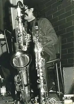 A 32-year-old man is shown in left profile, there is a brick wall behind him. He stares ahead, with a microphone to his right.