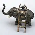 A black boy climbing up an elephant with a ladder. This one is identical to the lost figurine (NF.1914-0491).