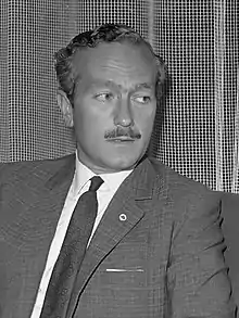 Colin Chapman in a black and white photograph sporting a mustache and looking to the left of the camera