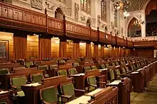 Photo of the back benches with wooden desks and chairs with green seats