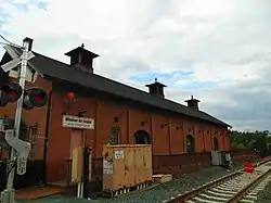 A one story brick building with a slanted roof adjacent to railroad tracks. Above the building's door is a sign reading "Windsor Art Center at the Freight House".