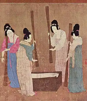 A painted image of four Chinese women wearing colorful silk robes, their hair tied up into buns, standing around a small wooden block with silk laid on top while holding large whisks which they use to beat the silk