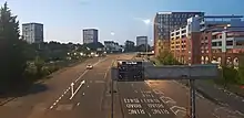 View of both carriageways and slip roads with a city centre car park on the right and tower blocks in the distance on the right