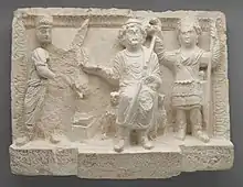 Limestone relief sculpture with three figures, the one on the right (in military dress) holding a crown over the head of the figure in the middle.