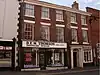 A red brick town house, in a terrace, seen from the north. A shop sign stretches across half the building and reads "D.E.M. Thomson".