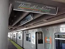 A metro train sits beside a station platform with its doors open.  A map of the metro system hangs from the roof of the station.