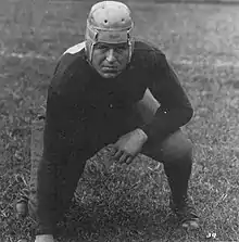 A Caucasoid man in a 1920s football helmet is posing poised for tackling.