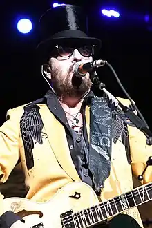 A color photograph of David A. Stewart, who is singing while wearing a golden tuxedo.