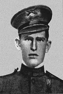 Face of a young man in military uniform. He has a stern expression and his hat, a peaked cap, is slightly cocked.