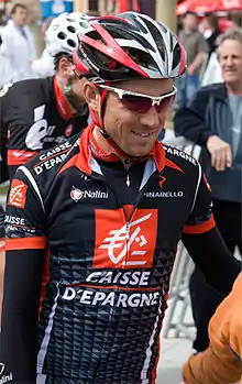 A road racing cyclist in a black and red jersey with white trim, and a matching helmet.