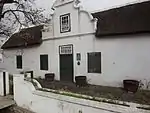 This house stands on the land bought from the Church by Jacob de Bruyn in 1796. It was probably built by Christiaan Willem Broodryk, who bought the top half in 1805. It is T-shaped, like no 22 Church St, with which it stands back to back. Its gable, preserved intact until the 1969 tremors made part of it collapse, is holbol but topped by a 3-lobed pediment with a vase on its face. The house had been restored previously – when it was turned into a library – but the sash windows which were then inserted were incorrect. The Simon van der Stel Foundation bought the house and had it restored. Type of site: House Previous use: Residential. Current use: House.