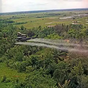 A UH-1D helicopter from the 336th Aviation Company sprays a defoliation agent over farmland in the Mekong Delta.