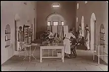 Sepia-toned photograph showing a room in a hospital with two seated patients being seen by medics.