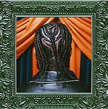 A photo of a Black man's head showing his braided hair. He's stood in front of blue and orange curtains, and the photo is surrounded by an ornate green photo frame.