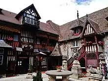 Interior view of the courtyard of the Village of Art Guillaume-le-Conquérant, with old stone and half-timbered buildings and a group of ancient sculptures.