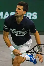 A brown-haired male tennis player with a white shirt and blue shorts