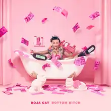 A photo of Doja Cat lying on a bathtub in a pink room, behind two statues of cats. Various money bills, also in pink, are shown either resting on the floor or flying mid-air. The name "Doja Cat" and the song title "Bottom Bitch" are printed in all caps at the bottom of the image.