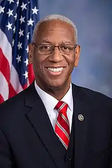 McEachin smiling, wearing a suit in front of an American flag