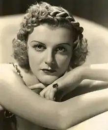 Black and white photo of a blonde woman leaning forward with her arms crossed in front of her