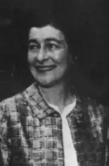 A smiling white woman with dark hair, wearing a print jacket over a white blouse