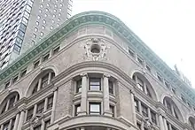 View of the curved corner's fifth through seventh stories. The fifth and sixth stories form a small colonnade. The seventh story has an oculus with terracotta decorations and cresting.