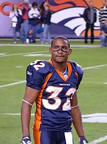 An American football player looks at the crowd. He is wearing his uniform on the field with some spectators in the background.