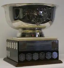 Large silver bowl engraved with a several designs mounted on a square wooden plinth adorned with engraved name plates of recipients