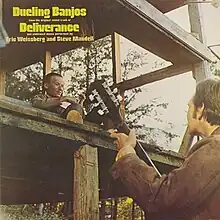 A photo of two men playing banjo facing one another: one seated on a porch several feet above the other