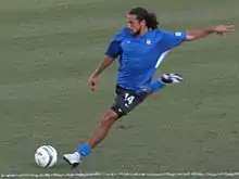 A young man wearing a blue soccer uniform beginning to kick a soccer ball on a soccer field