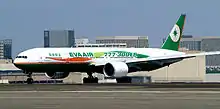 Side view of twin-jet aircraft on runway in front of airport buildings.