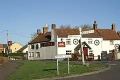 Road junction with direction sign. In the background is a white painted building with a pub sign saying The Crown.