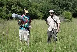 Two individuals recording. The one on the left is using a Zoom H4n with an external mic (and windscreen) plugged into one of the XLR inputs. The one on the right is using a Zoom H4.