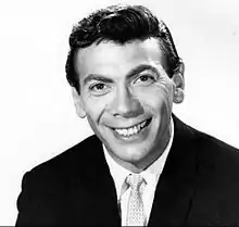 A dark-haired man in a jacket and tie, smiling broadly