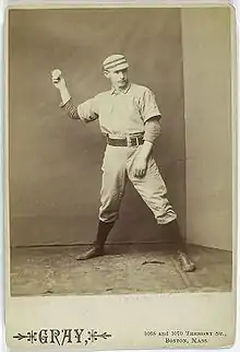 A sepia-toned baseball card image of a man in old-style white baseball pants, jersey, and cap pantomiming throwing a baseball with his right hand