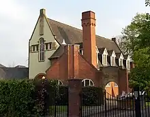 A rendered building with a cross-shaped window at the end, dormers along the sides with a red brick protruding wing and a tower