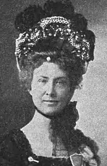 A white woman wearing a large, elaborate bonnet, tied under her chin with a mass of tulle.