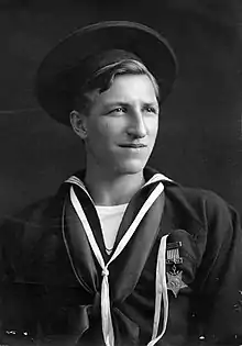 A young white man in a seaman uniform decorated with a star-shaped medal on the left breast, looking off into the distance.