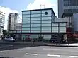 A light blue building with a dark blue sign reading "ELEPHANT & CASTLE STATION" in white letters all under a blue sky with white clouds