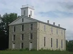 Three story gray rectangular building on a grassy hill