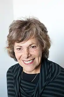 close-up of Ellen Langer wearing dark striped top with thin gold necklace, grinning at camera