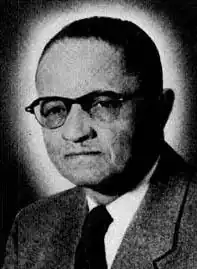 Grainy backlit formal photograph of a man wearing glasses in a suit and tie