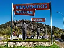 A sculpture depicting two Andalusians with banners reading "Bienvenidos", "Hola", "Welcome".