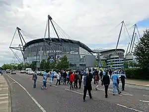 A grey stadium exterior with glass fronting. Adjoining it is a spiral walkway made of concrete, rising almost to the full height of the structure.